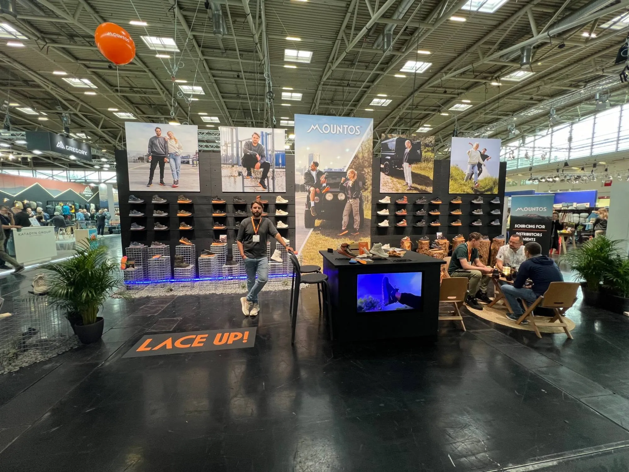 De Mountos-beursstand op de ISPO: een schoenenwand met campagnebeelden, LACE UP! op de vloer en een urban en een outdoor kant