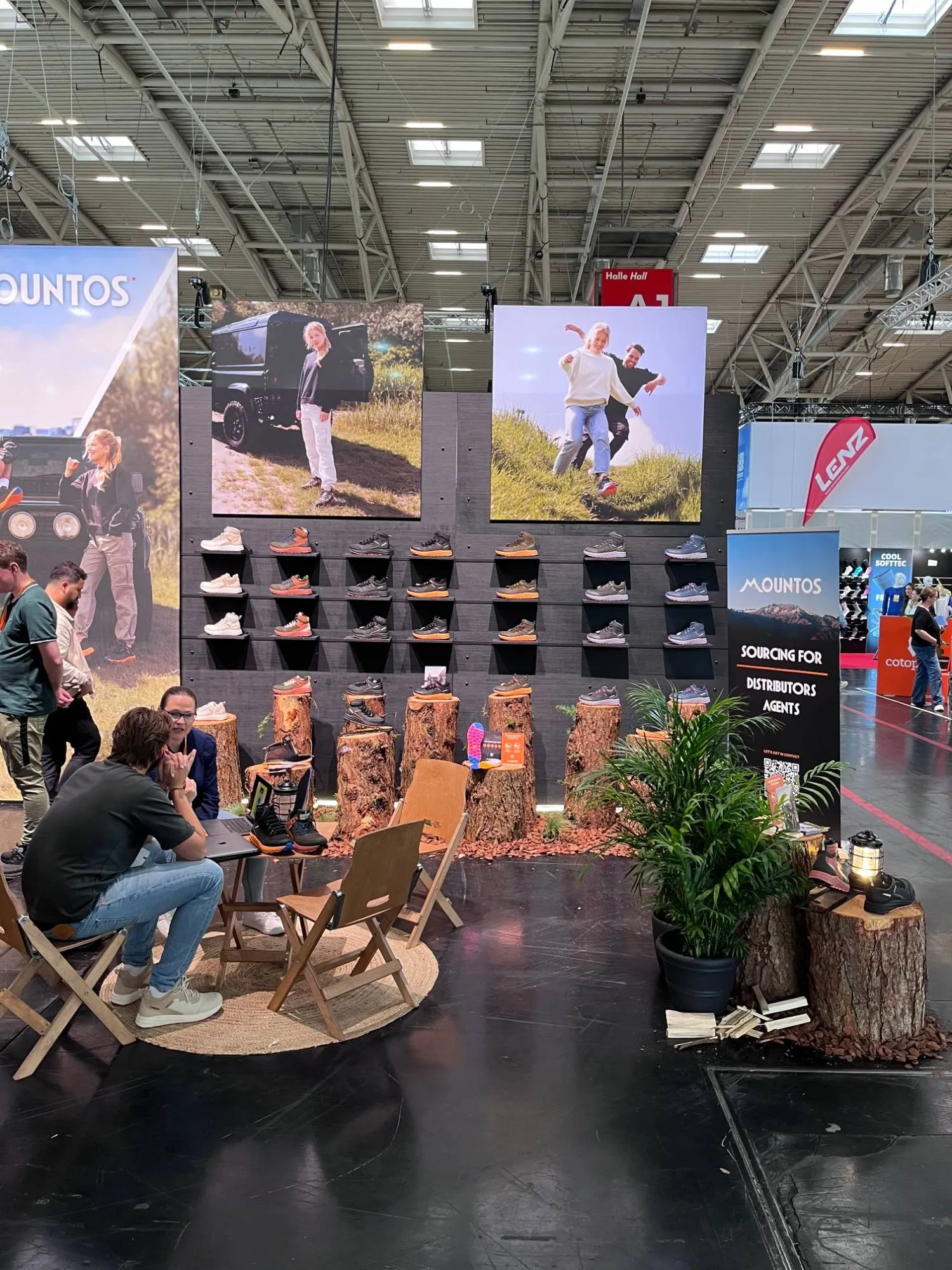 Gesprekken met bezoekers op houten klapstoelen aan de outdoor kant van de Mountos-stand